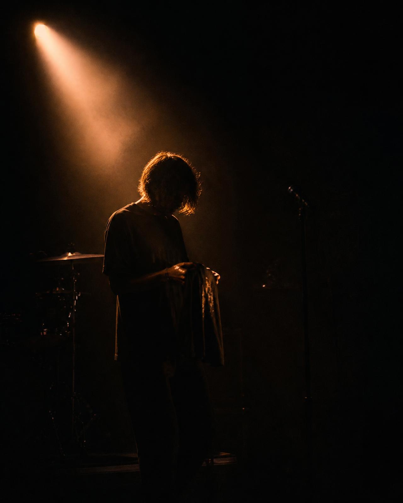 An independent artist on a dark stage holding a merch shirt